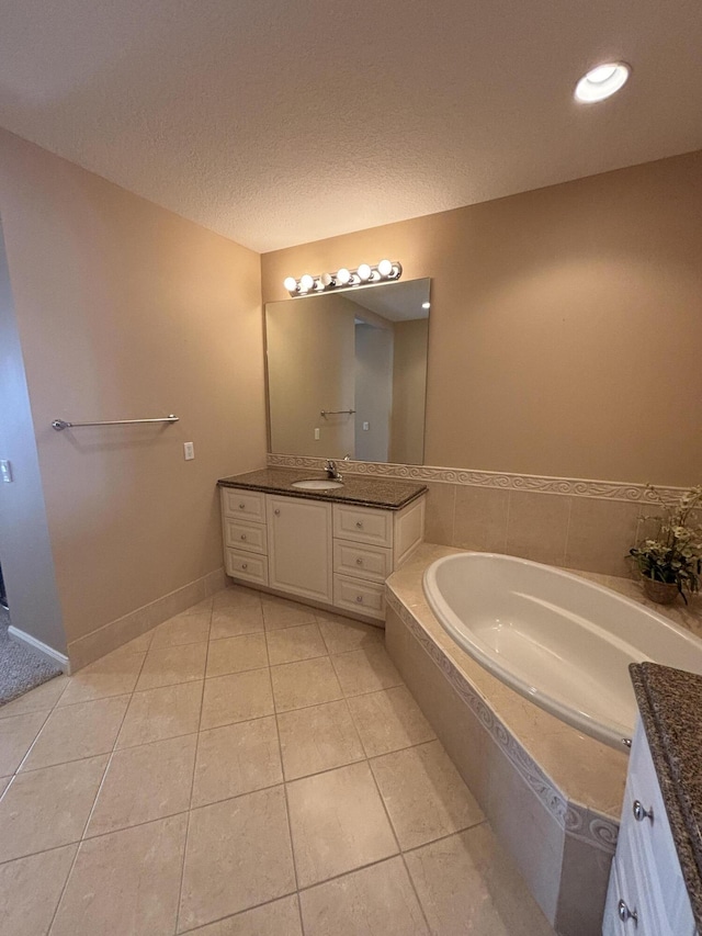 full bath featuring vanity, a garden tub, baseboards, a textured ceiling, and tile patterned floors