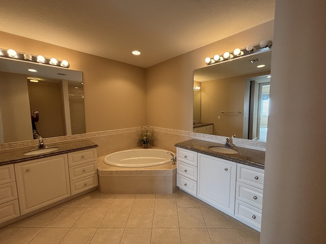 bathroom with tile patterned flooring, two vanities, a garden tub, and a sink