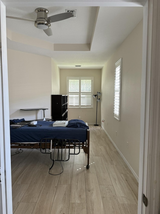 bedroom featuring a tray ceiling, baseboards, light wood-type flooring, and visible vents