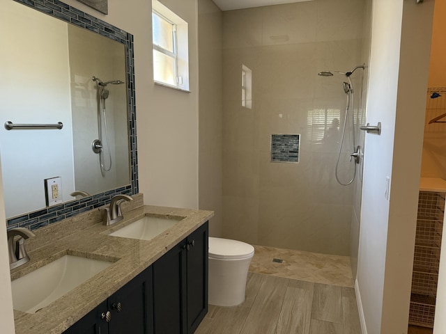 full bathroom featuring a sink, tiled shower, toilet, and double vanity