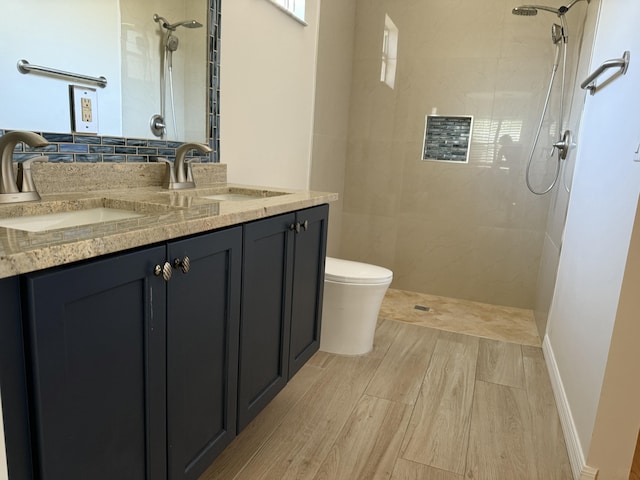 full bath featuring a sink, tiled shower, toilet, and double vanity