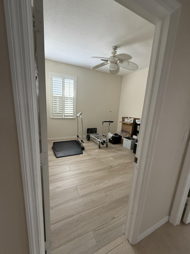 exercise area featuring a textured ceiling, baseboards, light wood-type flooring, and ceiling fan