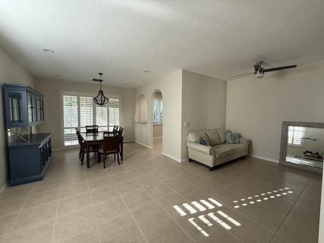 dining area featuring arched walkways, light tile patterned floors, a textured ceiling, and baseboards