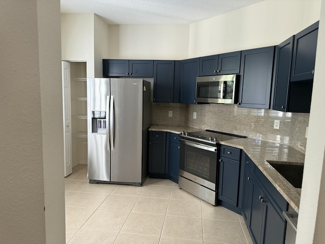 kitchen with light stone countertops, light tile patterned flooring, a sink, stainless steel appliances, and tasteful backsplash