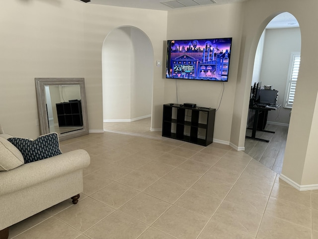 living area featuring light tile patterned floors, baseboards, and arched walkways