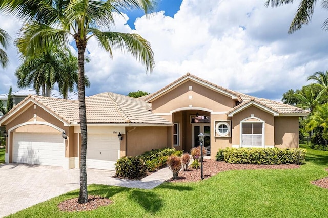 mediterranean / spanish-style home featuring a tiled roof, a garage, a front yard, and stucco siding