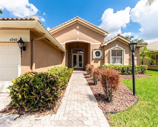 view of exterior entry with french doors, a garage, and stucco siding