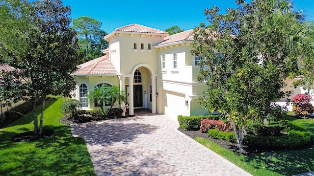 mediterranean / spanish-style house with stucco siding, decorative driveway, an attached garage, a front yard, and a tiled roof