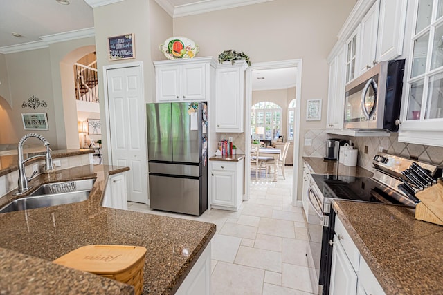 kitchen featuring arched walkways, ornamental molding, a sink, appliances with stainless steel finishes, and backsplash