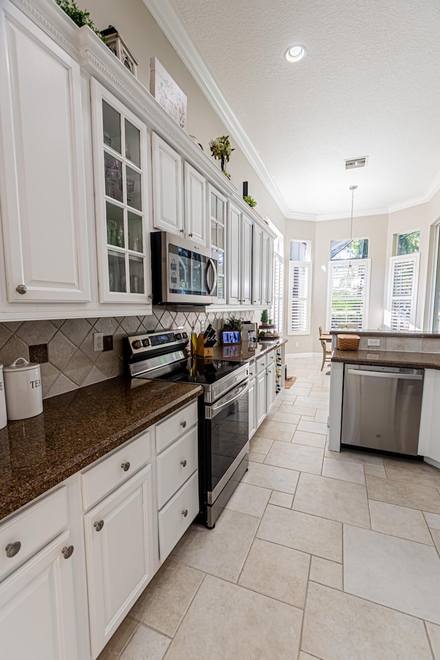 kitchen featuring visible vents, ornamental molding, backsplash, appliances with stainless steel finishes, and glass insert cabinets