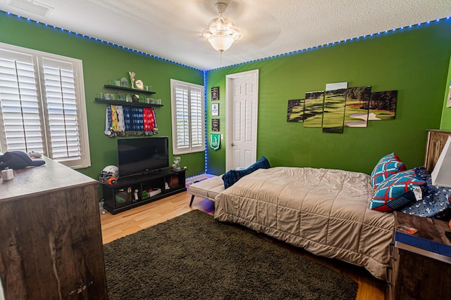 bedroom with visible vents, multiple windows, a textured ceiling, and wood finished floors