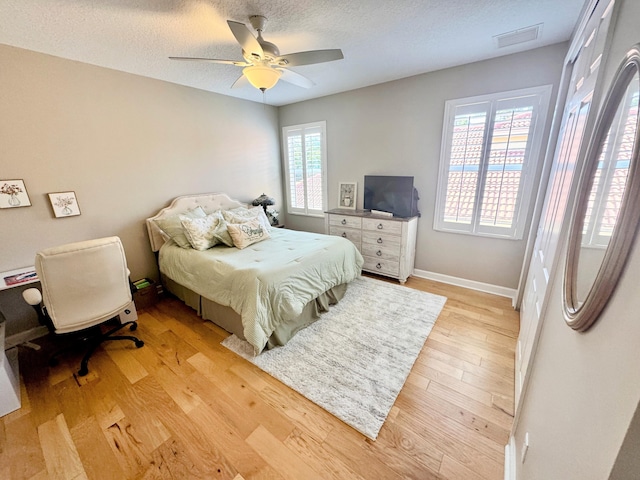 bedroom with a ceiling fan, baseboards, light wood-type flooring, and a textured ceiling