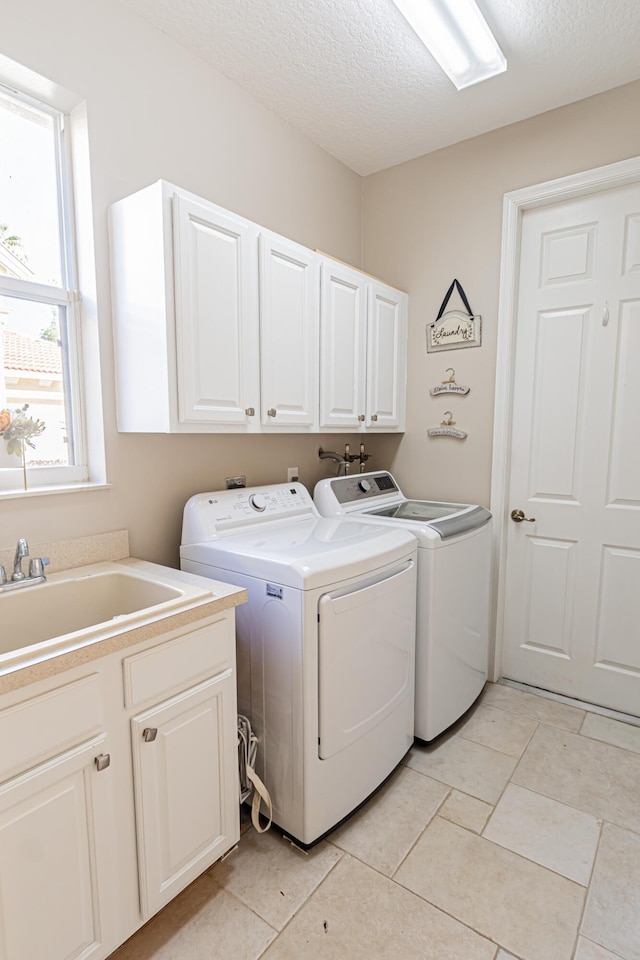 laundry area featuring a sink, a textured ceiling, washing machine and dryer, cabinet space, and light tile patterned floors