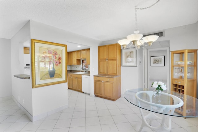 kitchen with visible vents, a sink, an inviting chandelier, white dishwasher, and baseboards