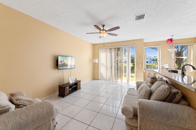 living area with light tile patterned floors, baseboards, visible vents, ceiling fan, and a textured ceiling