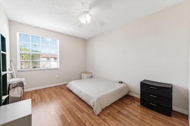 bedroom featuring light wood finished floors, ceiling fan, a textured ceiling, and baseboards