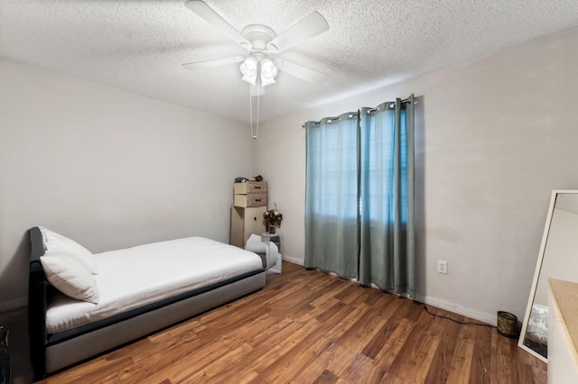 bedroom with ceiling fan, wood finished floors, baseboards, and a textured ceiling