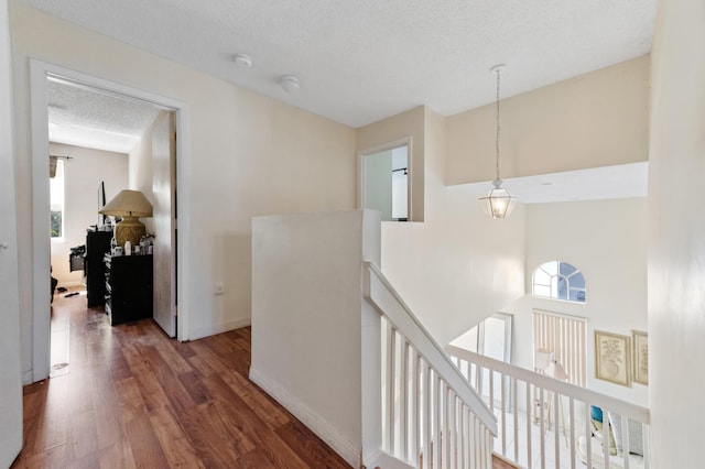 corridor featuring wood finished floors, an upstairs landing, baseboards, and a textured ceiling