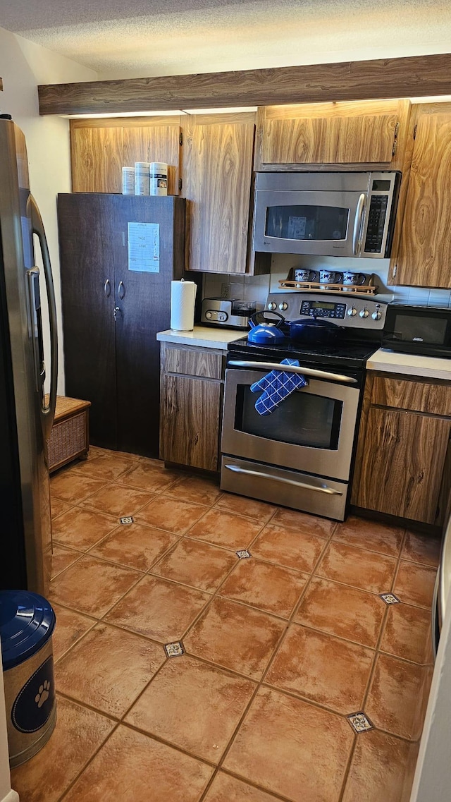 kitchen with light tile patterned flooring, a textured ceiling, light countertops, appliances with stainless steel finishes, and brown cabinetry