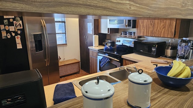 kitchen with light countertops, a sink, stainless steel appliances, and brown cabinetry