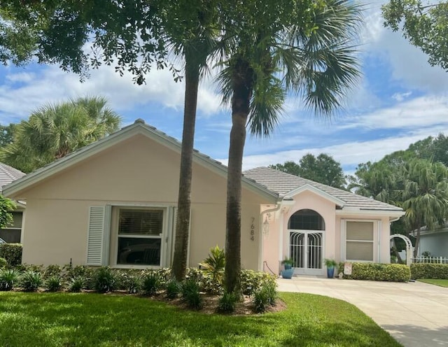 view of front of property featuring a tiled roof, stucco siding, french doors, and concrete driveway