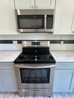 kitchen with light stone countertops, tasteful backsplash, light wood finished floors, and stainless steel appliances