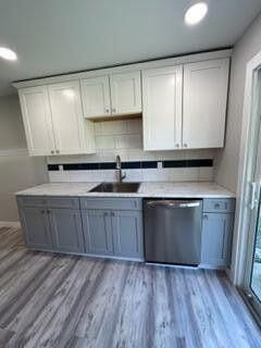 kitchen featuring light wood-style flooring, a sink, stainless steel dishwasher, white cabinets, and light countertops