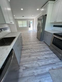 kitchen featuring light wood finished floors, a sink, stainless steel appliances, white cabinets, and open floor plan