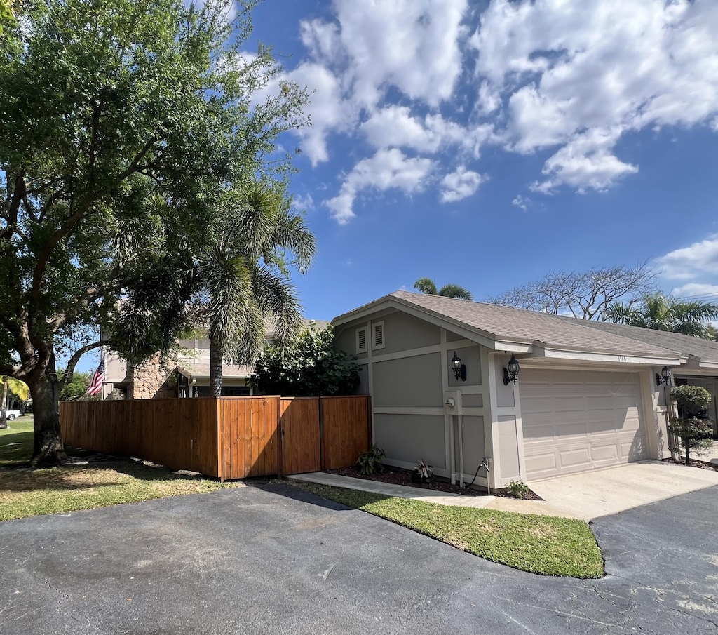 view of home's exterior featuring stucco siding, driveway, fence, a shingled roof, and a garage