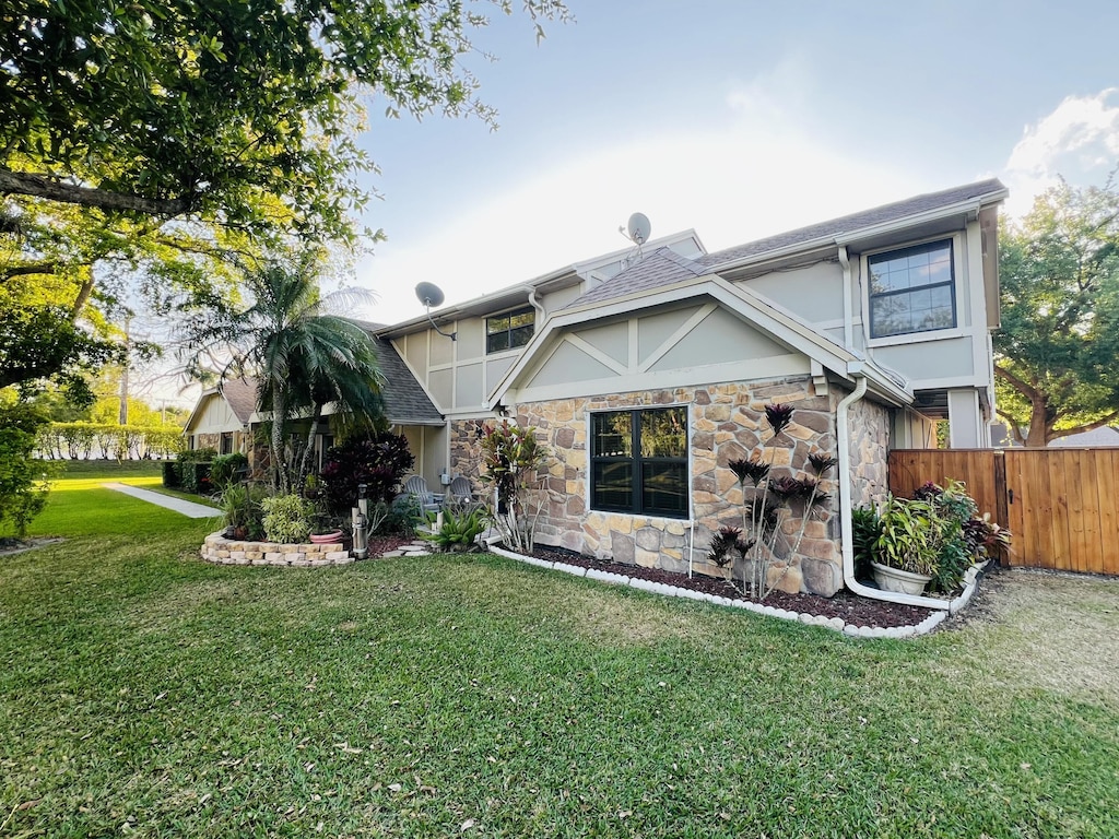 view of front of property featuring stucco siding, stone siding, a front yard, and fence