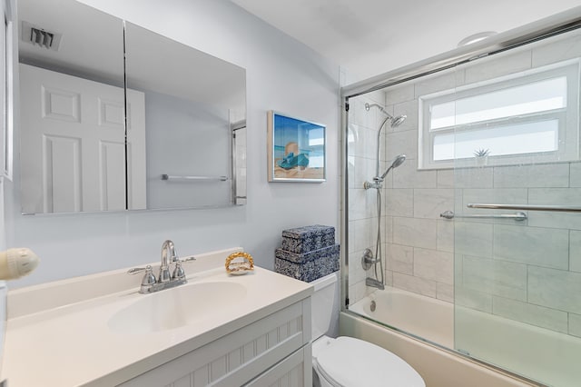 full bathroom with visible vents, toilet, vanity, and shower / bath combination with glass door