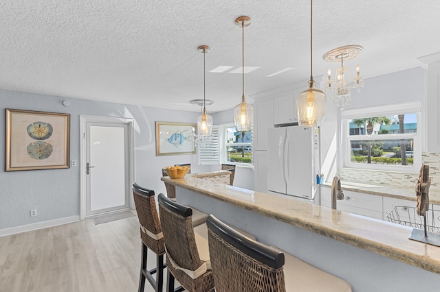 kitchen featuring a kitchen bar, a textured ceiling, freestanding refrigerator, light wood finished floors, and light stone countertops