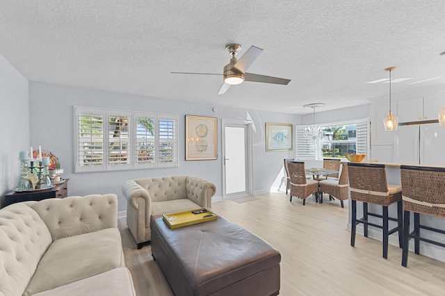 living room with light wood-style flooring, a ceiling fan, baseboards, and a textured ceiling