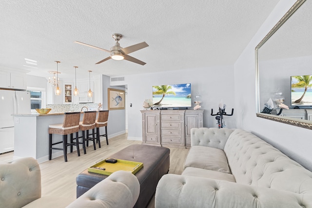 living area with light wood finished floors, visible vents, a textured ceiling, and ceiling fan