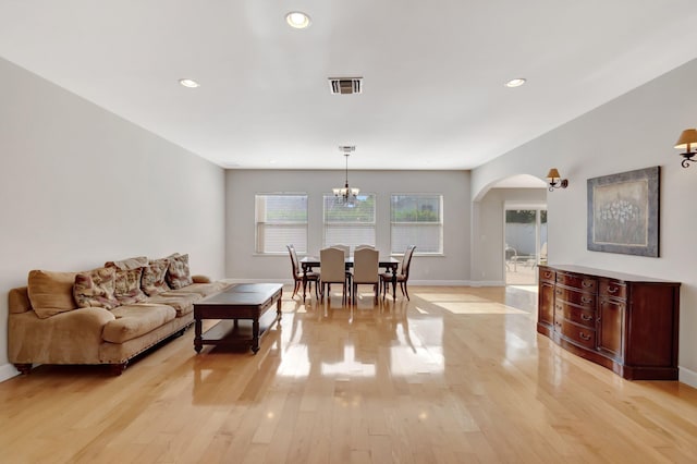 living area featuring light wood-style floors, arched walkways, a chandelier, baseboards, and visible vents