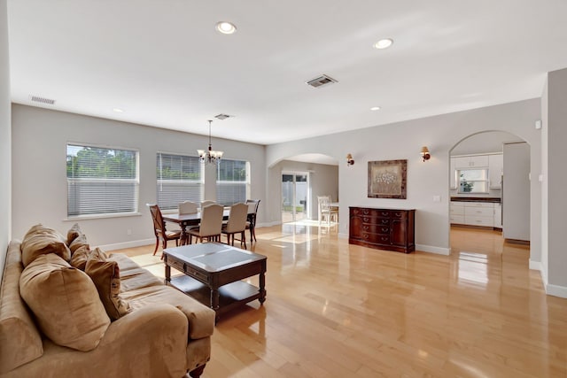living area with an inviting chandelier, arched walkways, a wealth of natural light, and visible vents