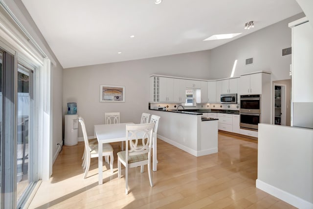 kitchen with white cabinets, stainless steel appliances, a skylight, and light wood finished floors