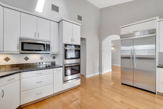 kitchen with a high ceiling, arched walkways, stainless steel appliances, decorative backsplash, and visible vents