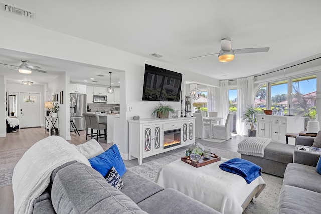 living room with light wood finished floors, visible vents, and a ceiling fan
