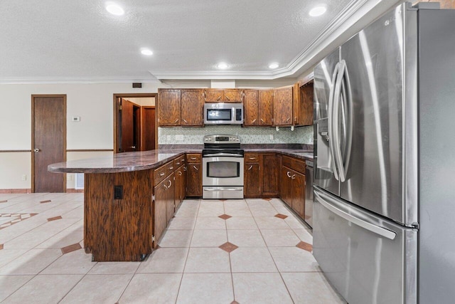 kitchen with backsplash, ornamental molding, appliances with stainless steel finishes, a peninsula, and light tile patterned flooring