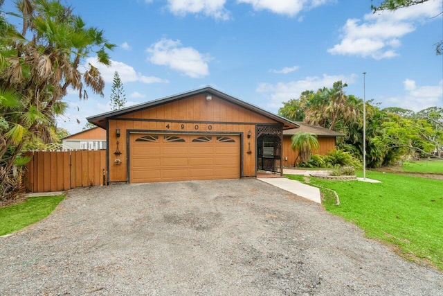 view of front facade featuring a garage, gravel driveway, a front lawn, and fence