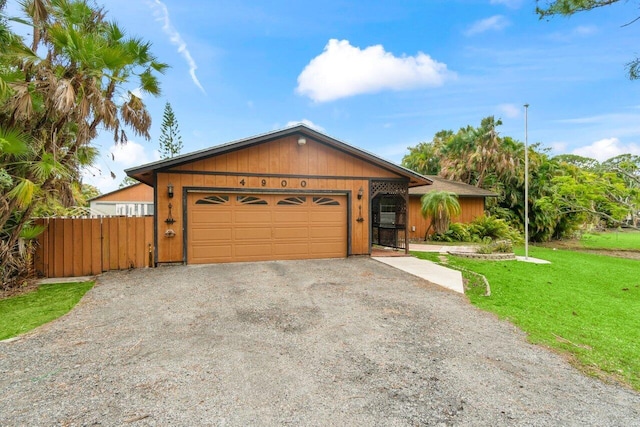 view of front of property with an attached garage, gravel driveway, a front lawn, and fence