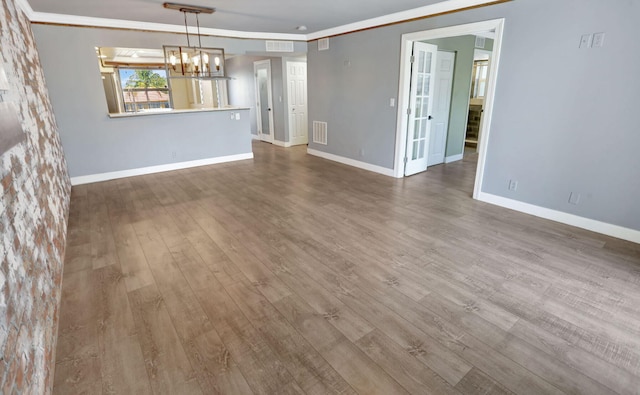 unfurnished dining area featuring wood finished floors, visible vents, crown molding, baseboards, and a notable chandelier
