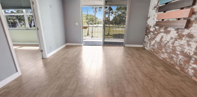 spare room with brick wall, baseboards, and wood finished floors