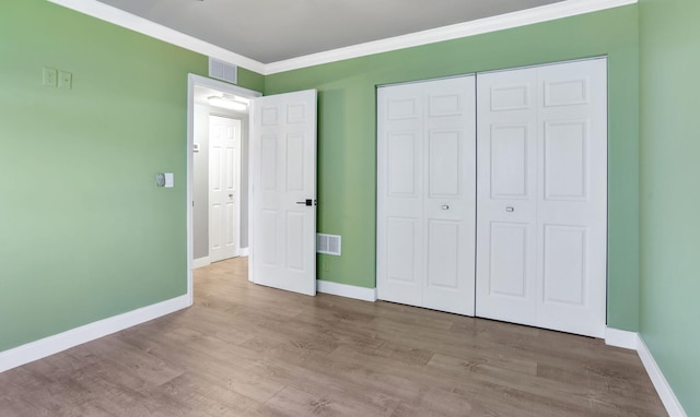 unfurnished bedroom featuring baseboards, wood finished floors, visible vents, and ornamental molding