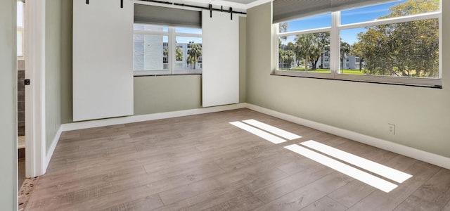 unfurnished room with a barn door, baseboards, and wood finished floors