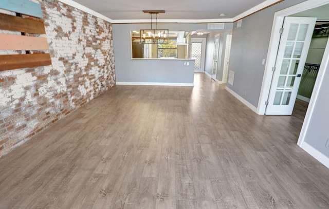 interior space with ornamental molding, wood finished floors, brick wall, and a chandelier