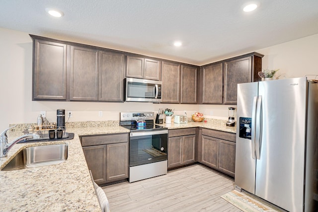 kitchen featuring light stone countertops, light wood finished floors, a sink, dark brown cabinetry, and appliances with stainless steel finishes