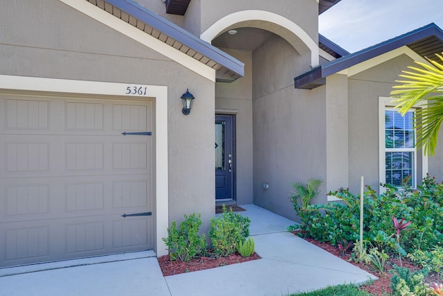 entrance to property featuring stucco siding, an attached garage, and concrete driveway