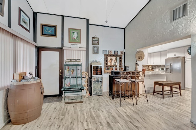 kitchen featuring visible vents, light wood finished floors, stainless steel fridge with ice dispenser, a towering ceiling, and white cabinetry